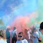 Blue, green and pink dust fill the sky as people in white t-shirts stand in a park.