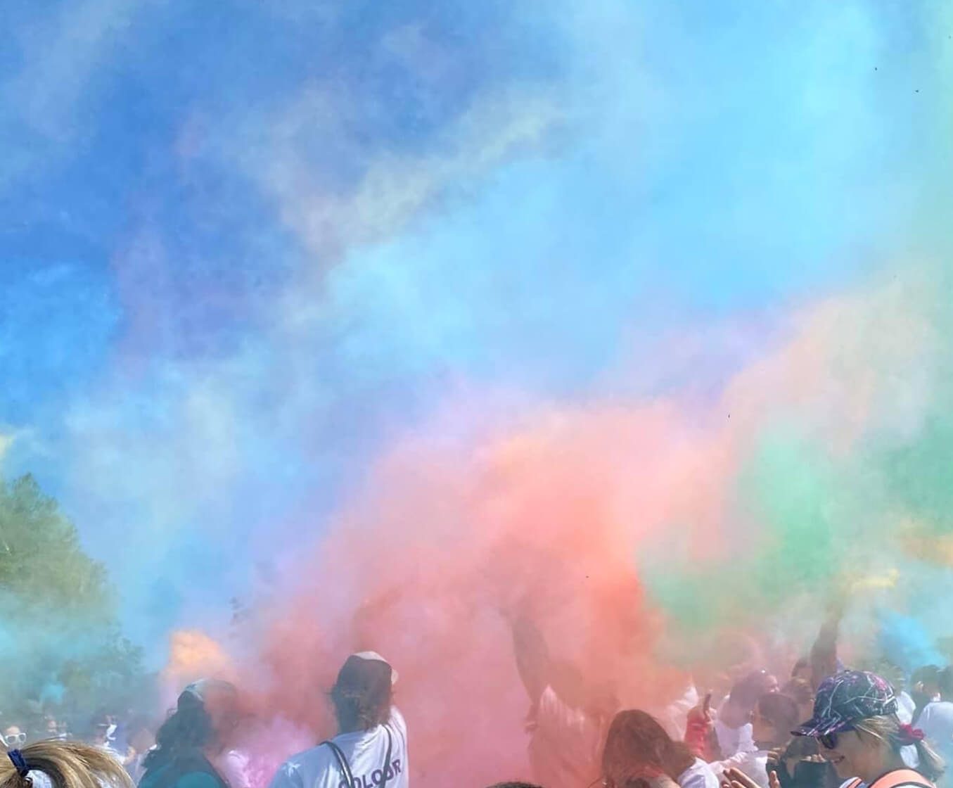 Blue, green and pink dust fill the sky as people in white t-shirts stand in a park.