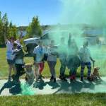 A group of people and two dogs in white t-shirts stands on a sidewalk surrounded by grass. Teal powder surrounds them in the sky.