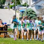 A group of people stand in a park in previously white shirts which have been stained with green and blue dye.
