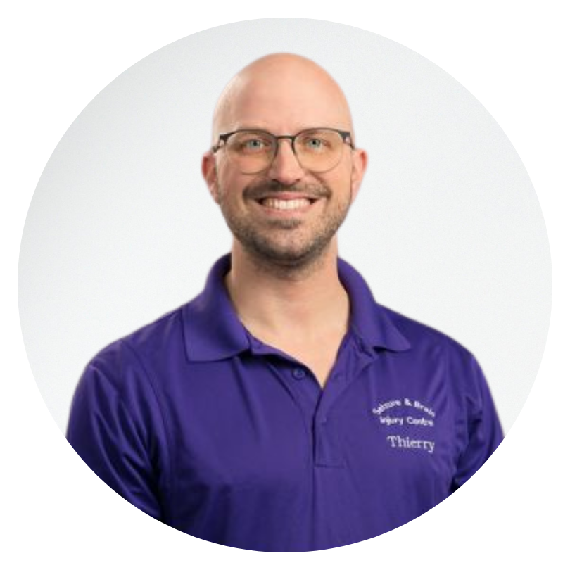 A portrait of a bald man in a purple shirt and glasses smiling at the camera